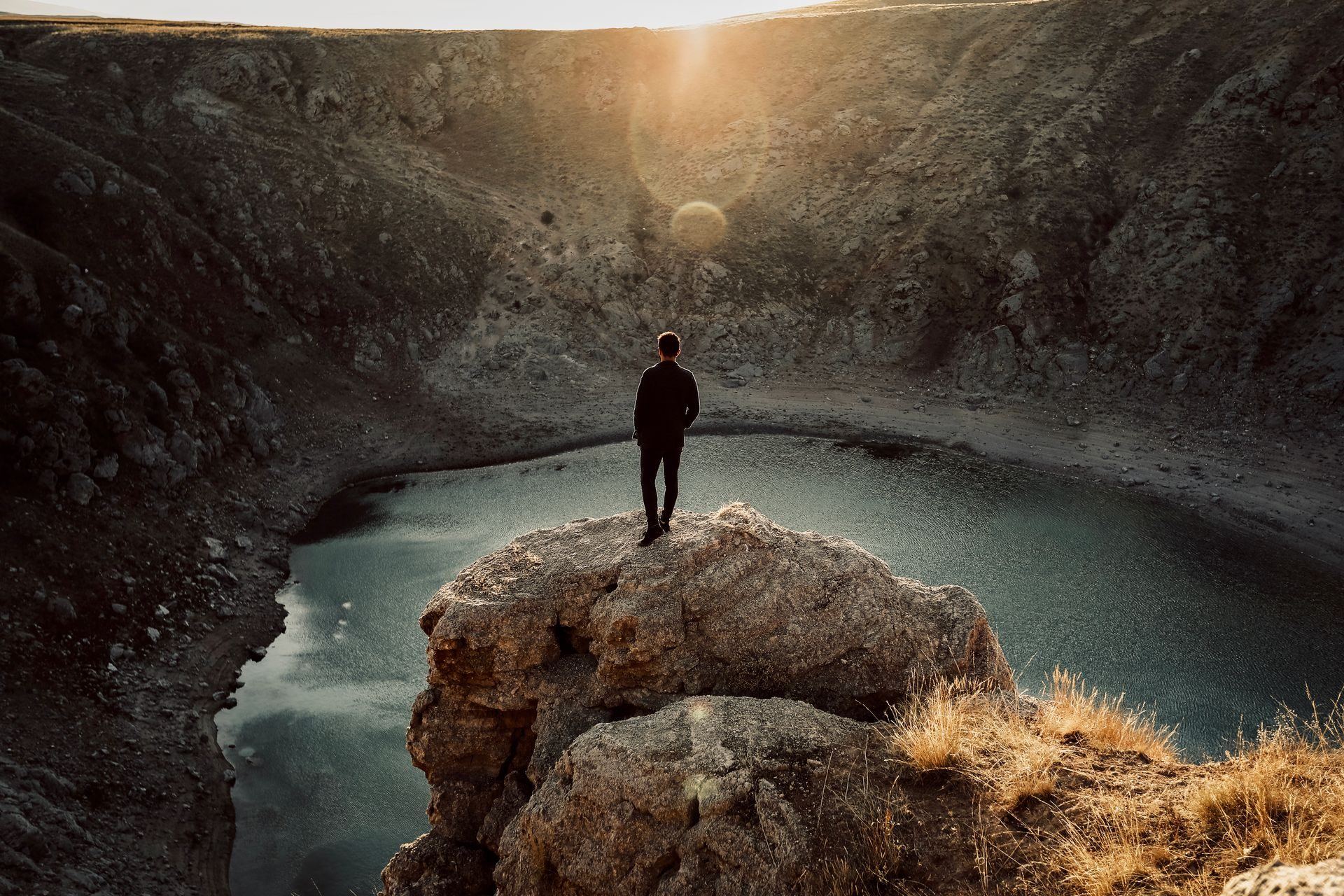 A man looking across a calm lake from a cliff